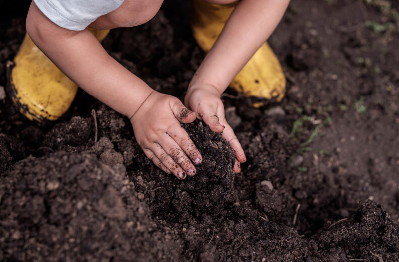 A child wearing yellow rain boots making a mound out of dirt.