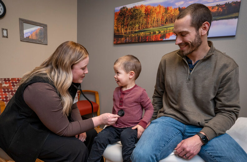 Family Medicine resident listening to the the stomach of a child with a stethoscope, while the father looks on.