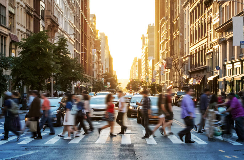 Group of people walking on a cross walk in a busy city.