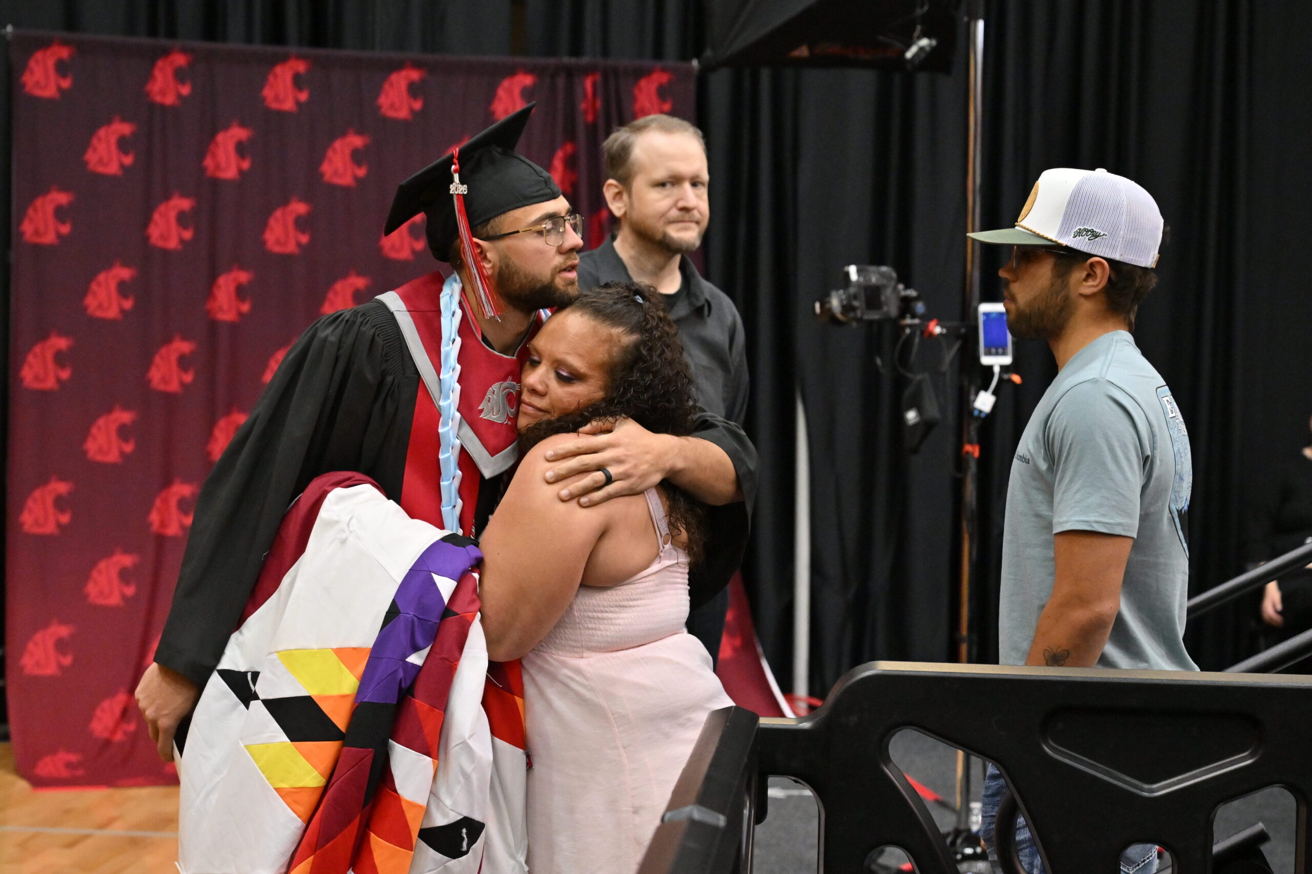 Graduate hugs another person near the stage during a graduation ceremony.