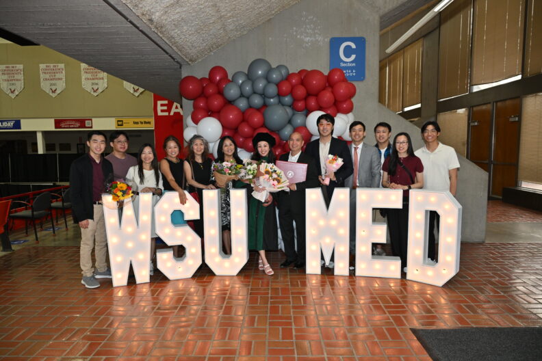 Group posing behind large illuminated “WSU MED” letters indoors.