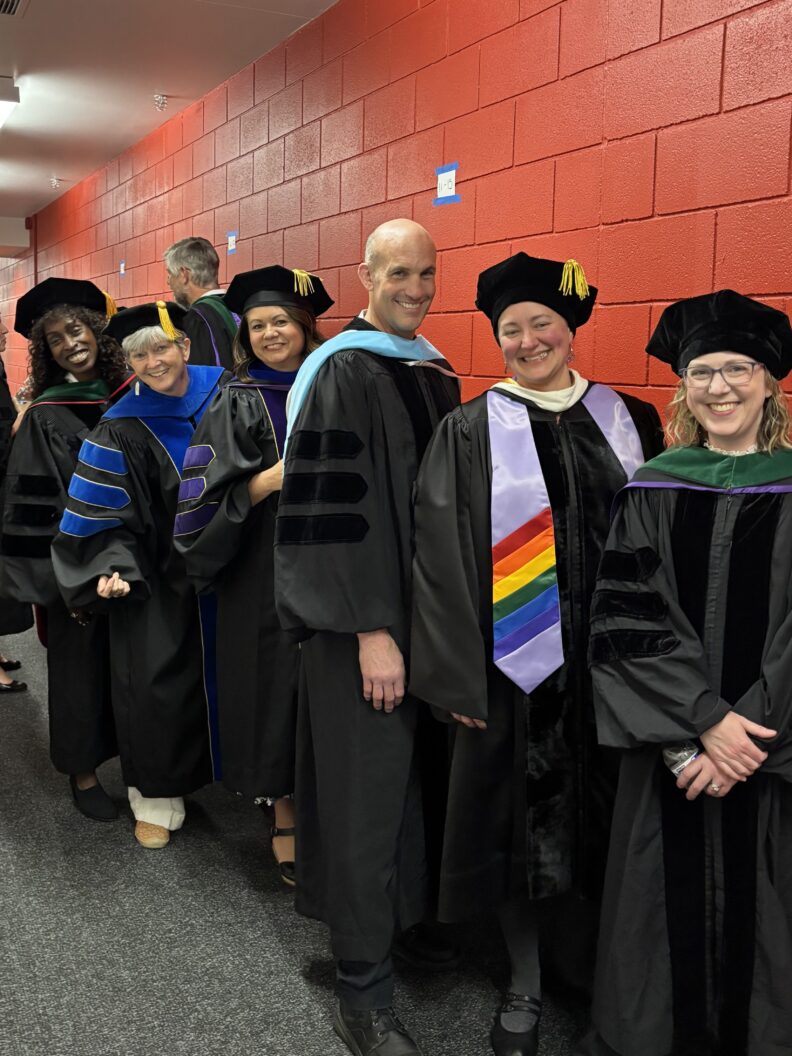 Line of people in regalia standing along a red hallway.