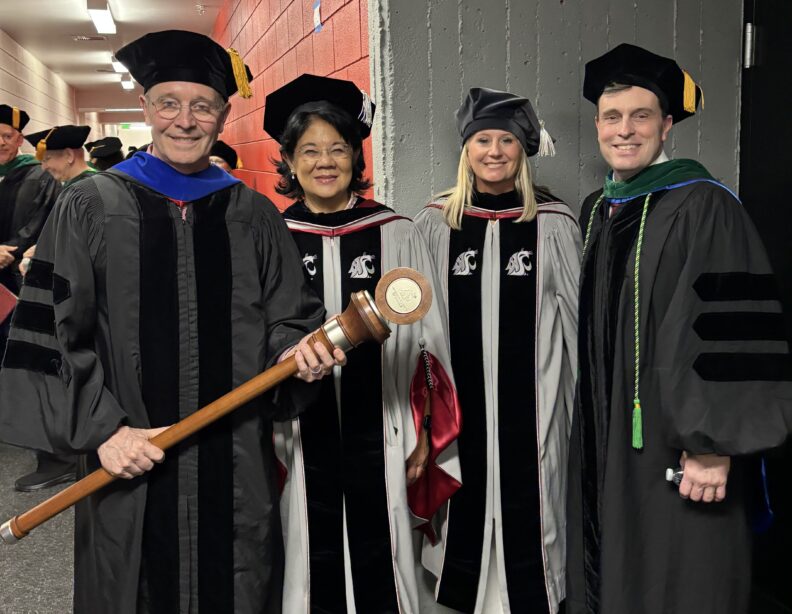 Four faculty members in regalia pose together, one holding a ceremonial mace.