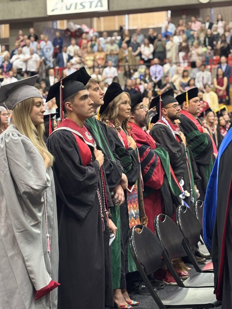 Graduates in regalia with their hands on their heart.