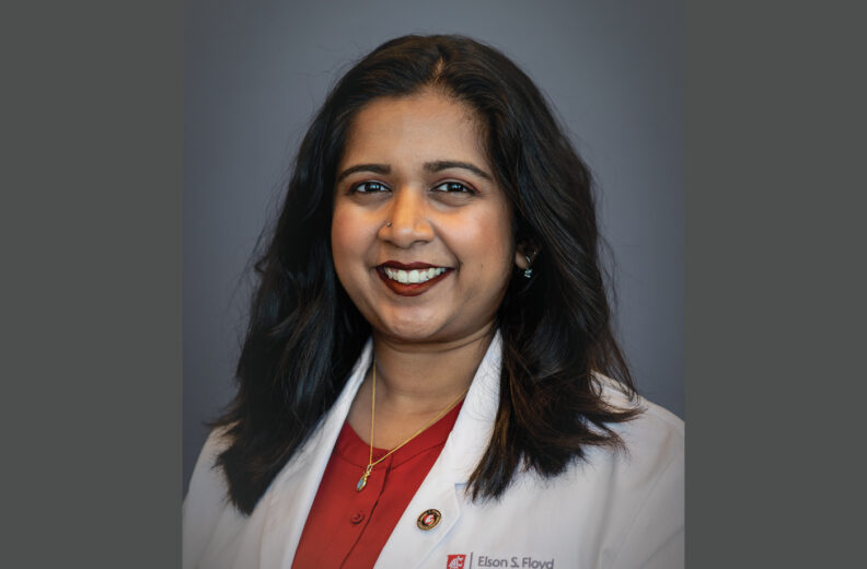 Headshot of a person wearing a white medical coat over a red shirt, smiling at the camera against a plain gray background, with a Washington State University Elson S. Floyd College of Medicine logo visible on the coat.
