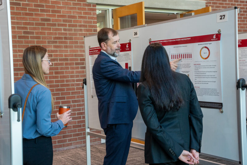 Faculty member points to a research poster while discussing findings with attendees.
