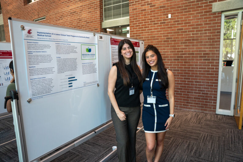 Two students stand smiling beside their research poster display.