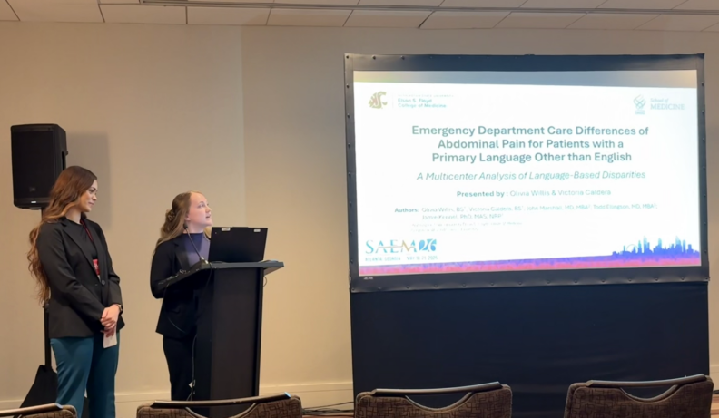 Two people are standing at a podium presenting a screen that says "Emergency Department Care Differences of Abdominal Pain for Patients with a Primary Language Other than English.".