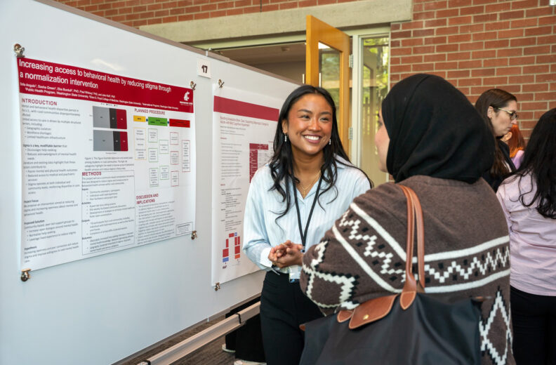 Student presents a research poster and speaks with an attendee during a campus research event.