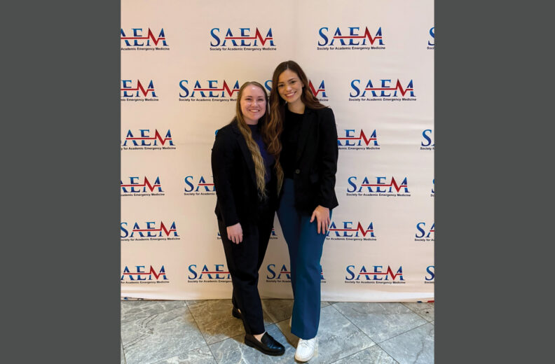 Two people smiling standing in front of a backdrop that says "SAEM".