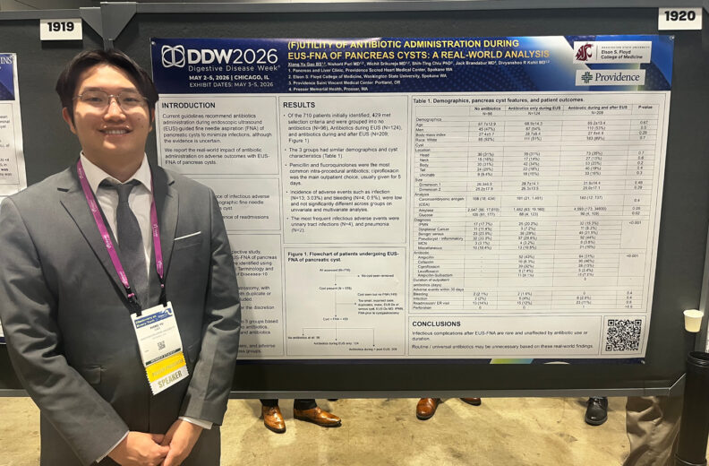 Person wearing a suit and conference badge standing beside a medical research poster display at a conference.