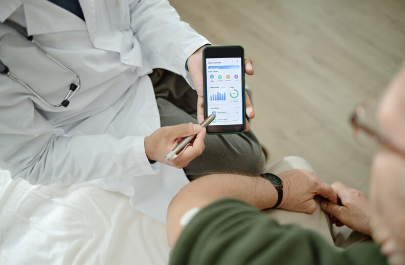 Healthcare professional shows a patient a smartphone app displaying glucose monitoring data and progress charts.