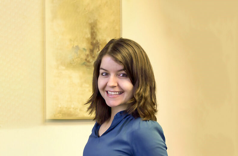 A women smiling in front of a yellow wall.