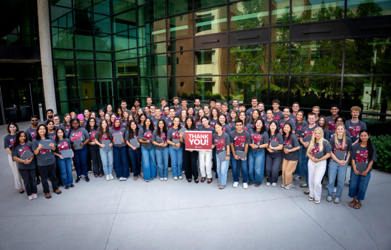 The full class of 2030 standing outside the College of Medicine building holding their ipads and stethoscopes and a sign that says thank you.