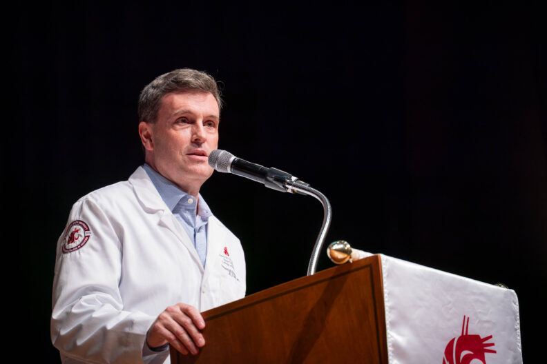 A man standing in his White Coat speaking into a mic.