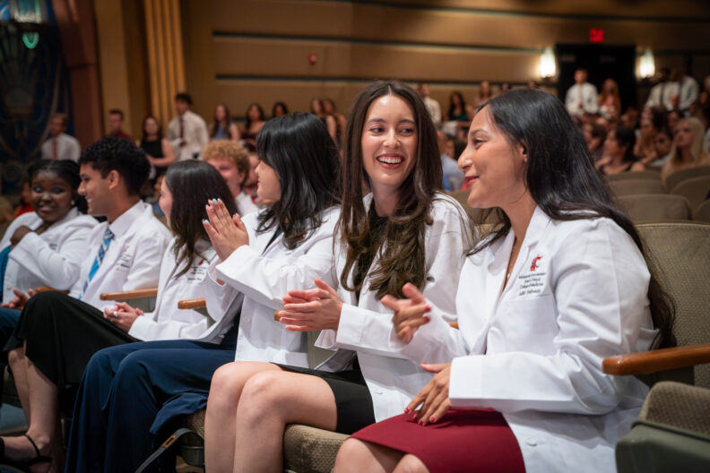 Two students wearing their White Coats smiling and chatting.