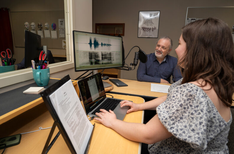 Researcher looking a computer of a speech test while a patient looks on.