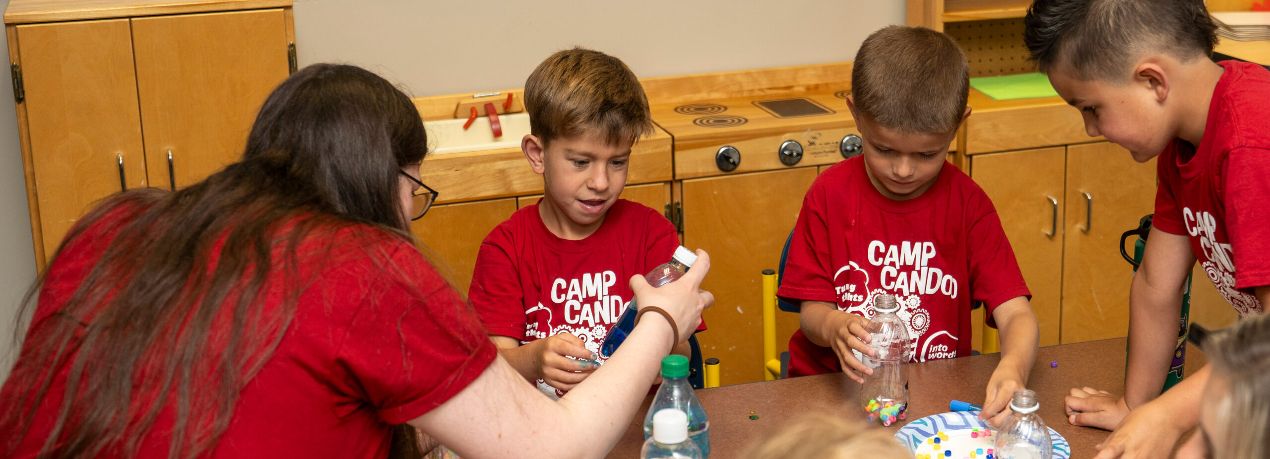 Graduate student with 3 camp candoo children building crafts.