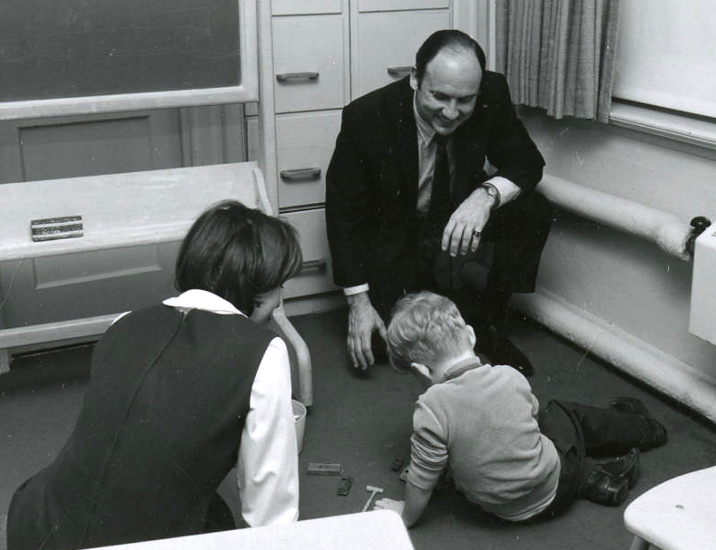 1970 photo of two instructors playing with a child in the hearing lab.