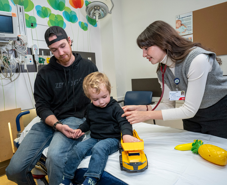 Pediatric Resident listening to child's breath while father looks on.