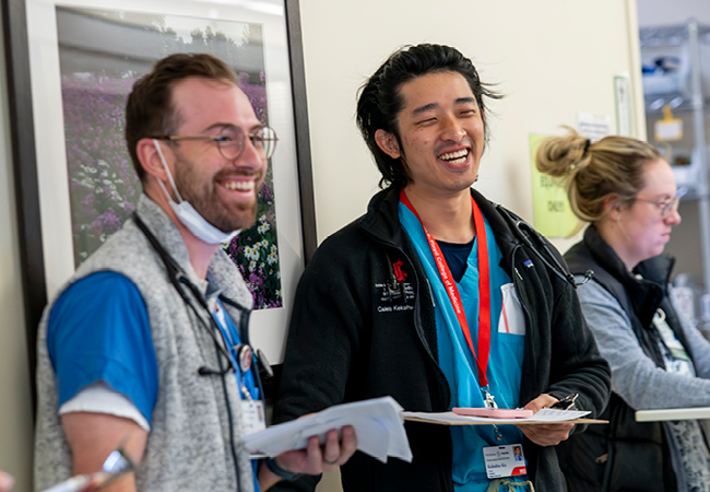 Two doctors holding charts and smiling in hospital hallway.