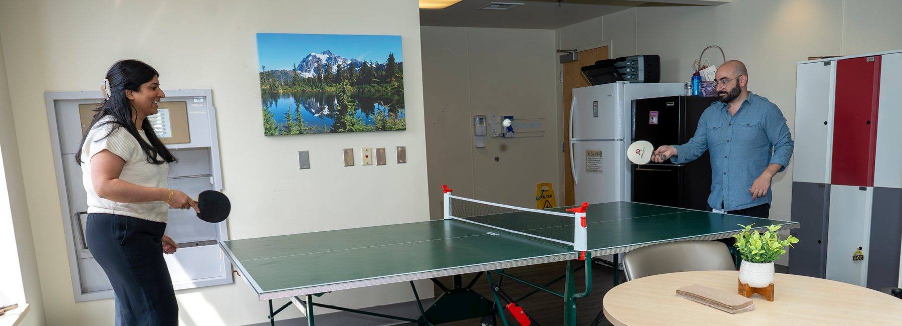 Two residents playing ping pong in the break room.