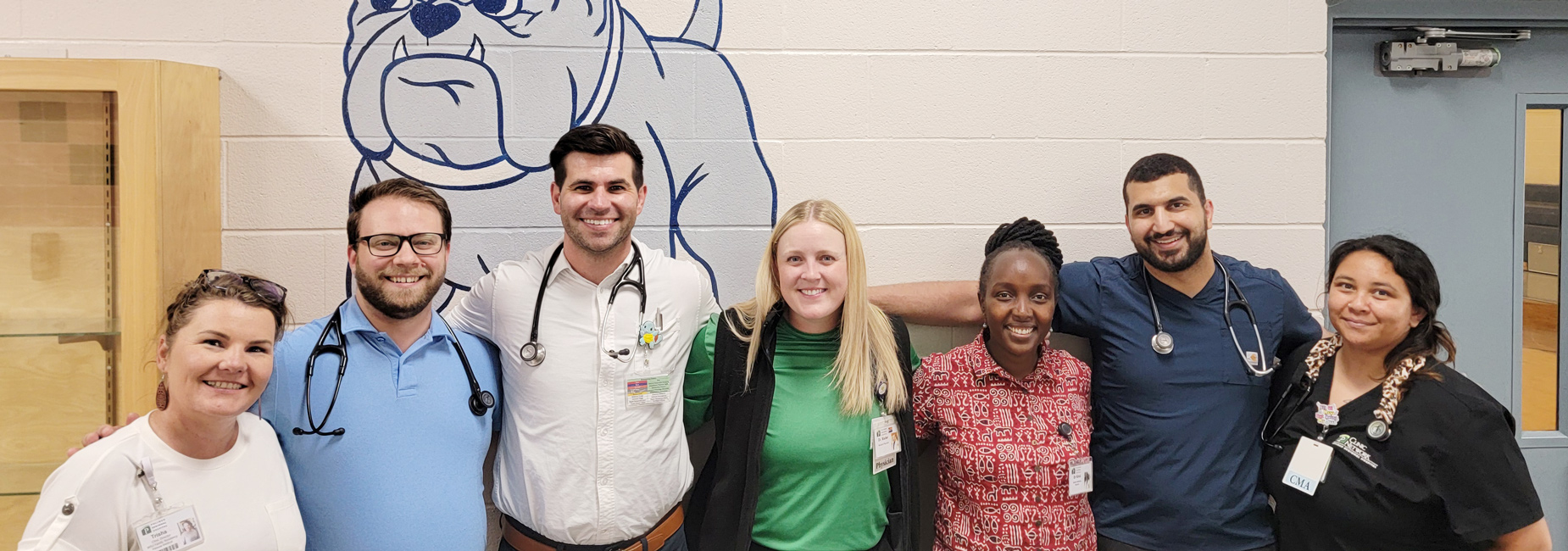 Group of 7 residents and doctors standing outside a local high school gym.