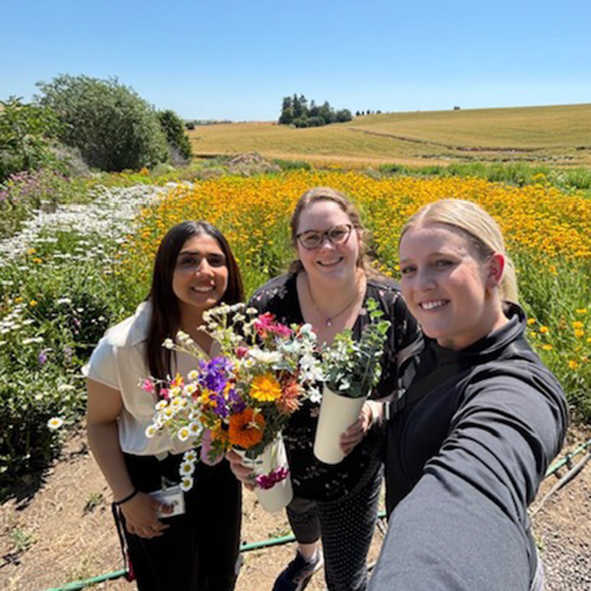 3 residents outside on the Palouse, picking wild flowers.