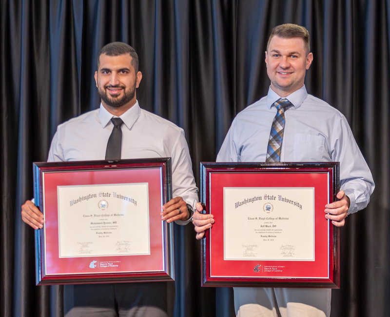 Two family medicine residents holding their framed graduation diplomas. 