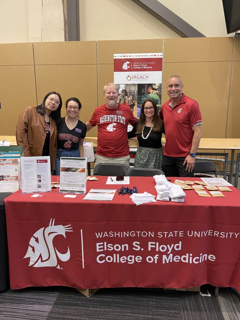IREACH faculty and staff standing behind a trade table at an event.