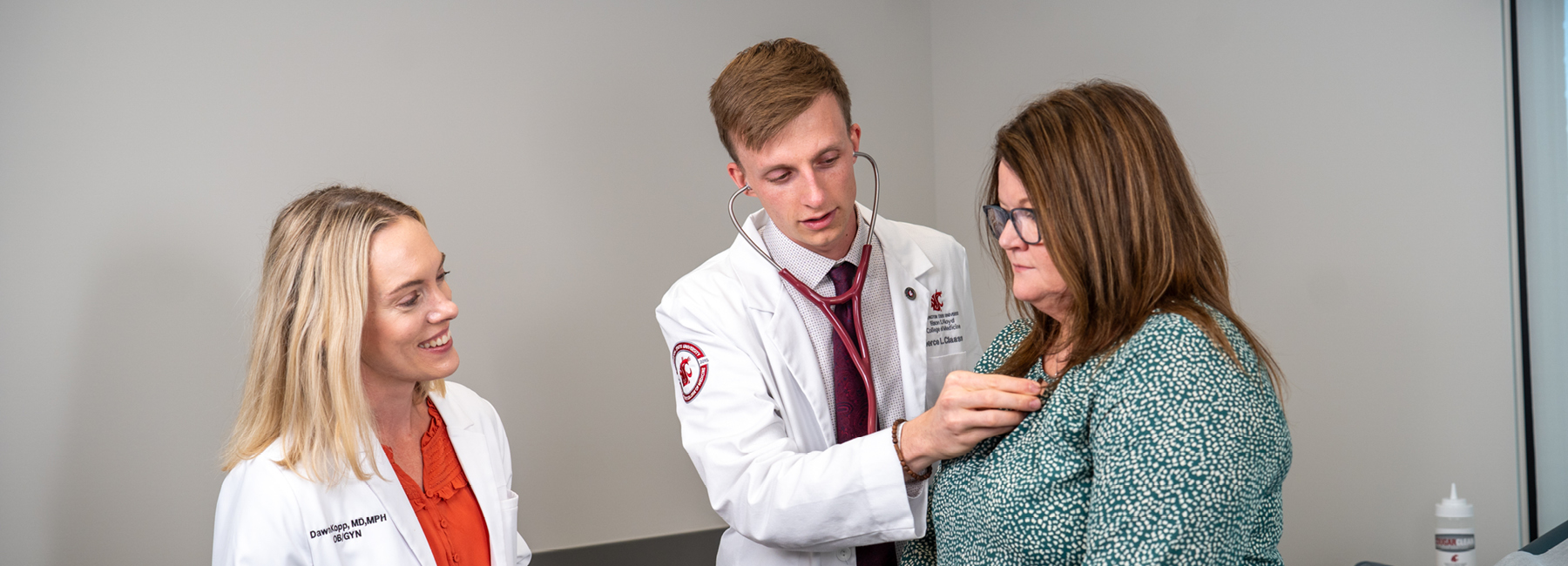 Medical student checking heart beat of a patient, while professor observes