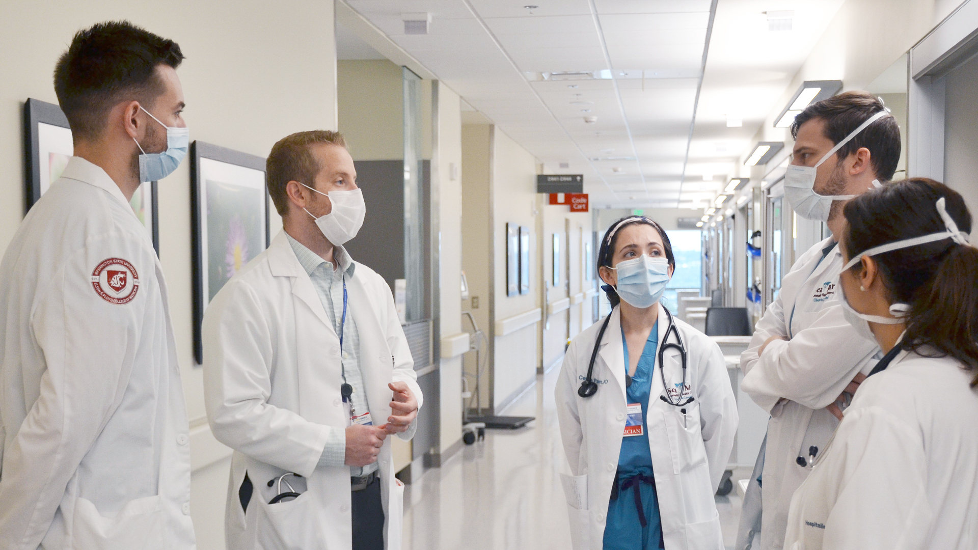 Group of first year residents in the hospital hallway talking to program director. 