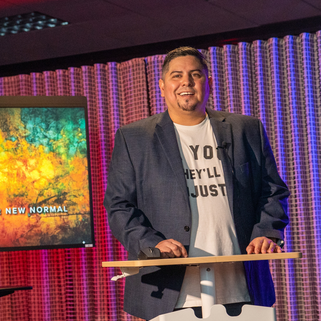 David Garcia standing at a podium with a tv behind him, speaking at a virtual conference.