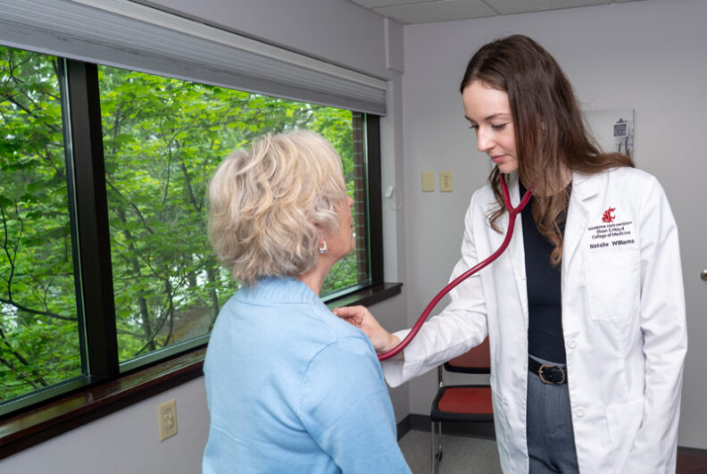 MD student checking the heart rate of an elderly patient in an exam room.
