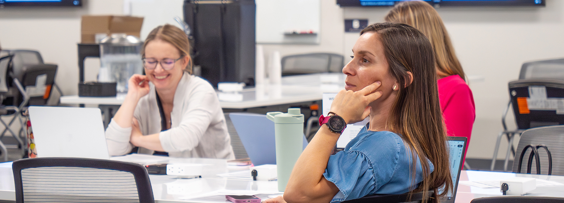 Three faculty members sitting at a table listening to a presentation.