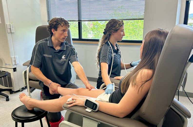 Two graduate students doing an ultra sound on a patient as they sit in a chair.