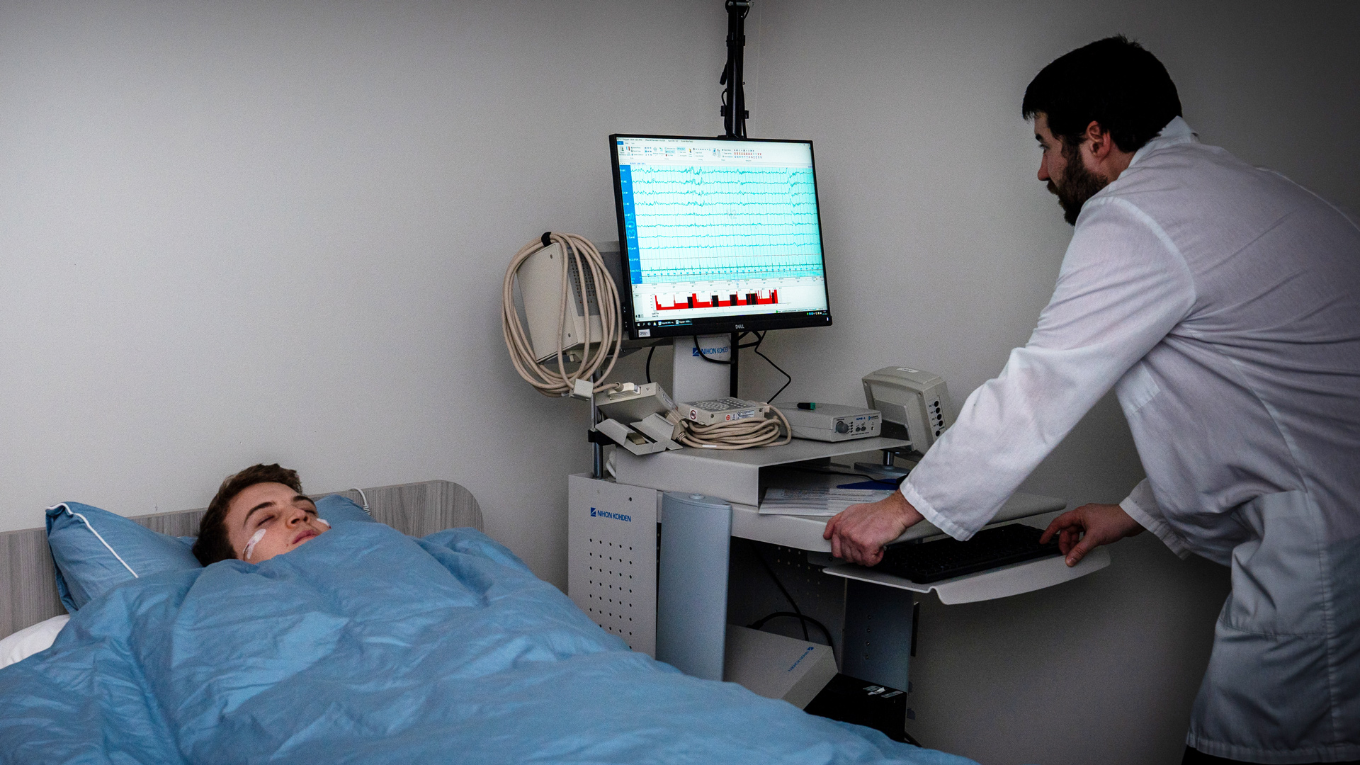 Adult sleeping in bed, while a researcher is reading the results on a computer next to them.