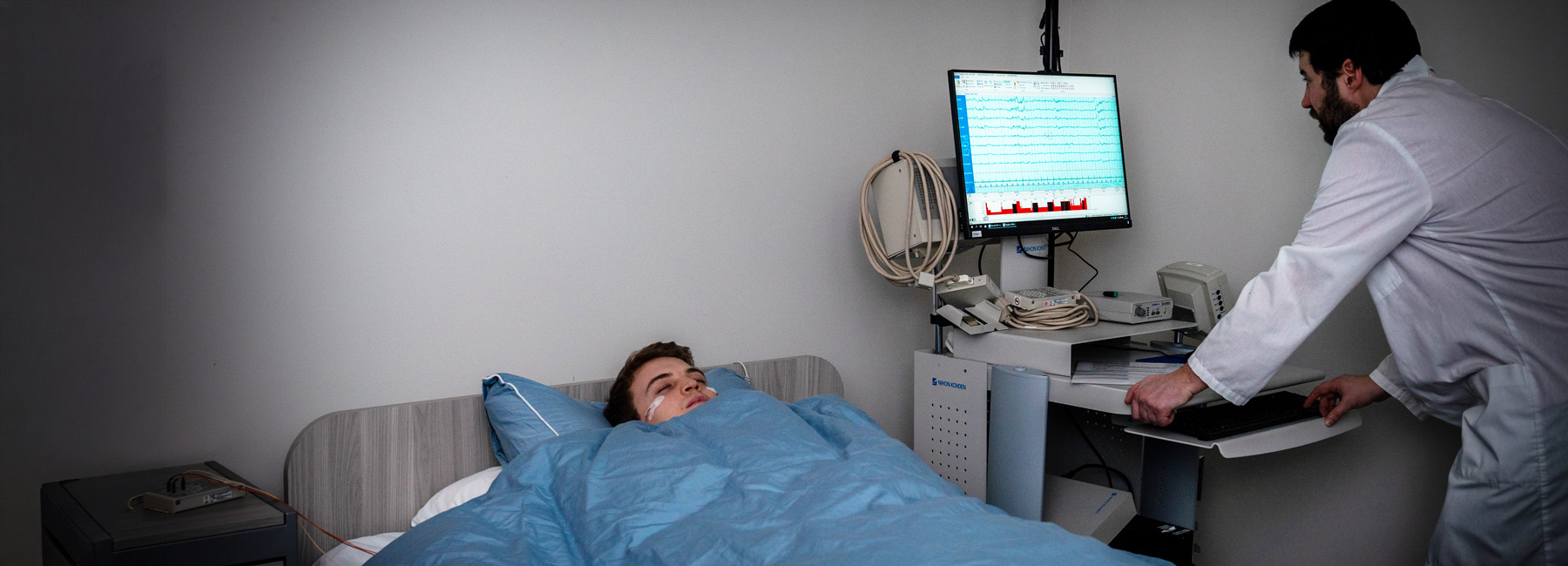 Adult sleeping in bed, while a researcher is reading the results on a computer next to them.