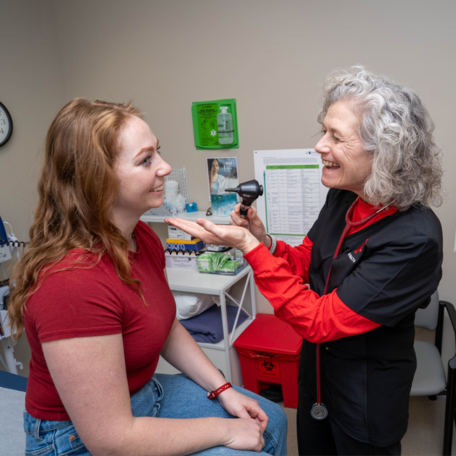 Nurse getting ready to look into the mouth of a student in an exam room.