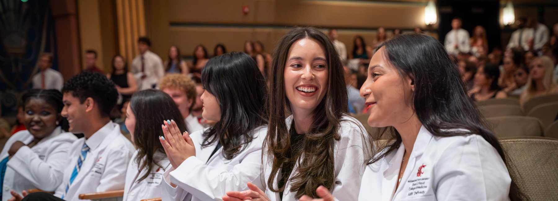 Smiling students sitting in the theater during White Coat Ceremony.