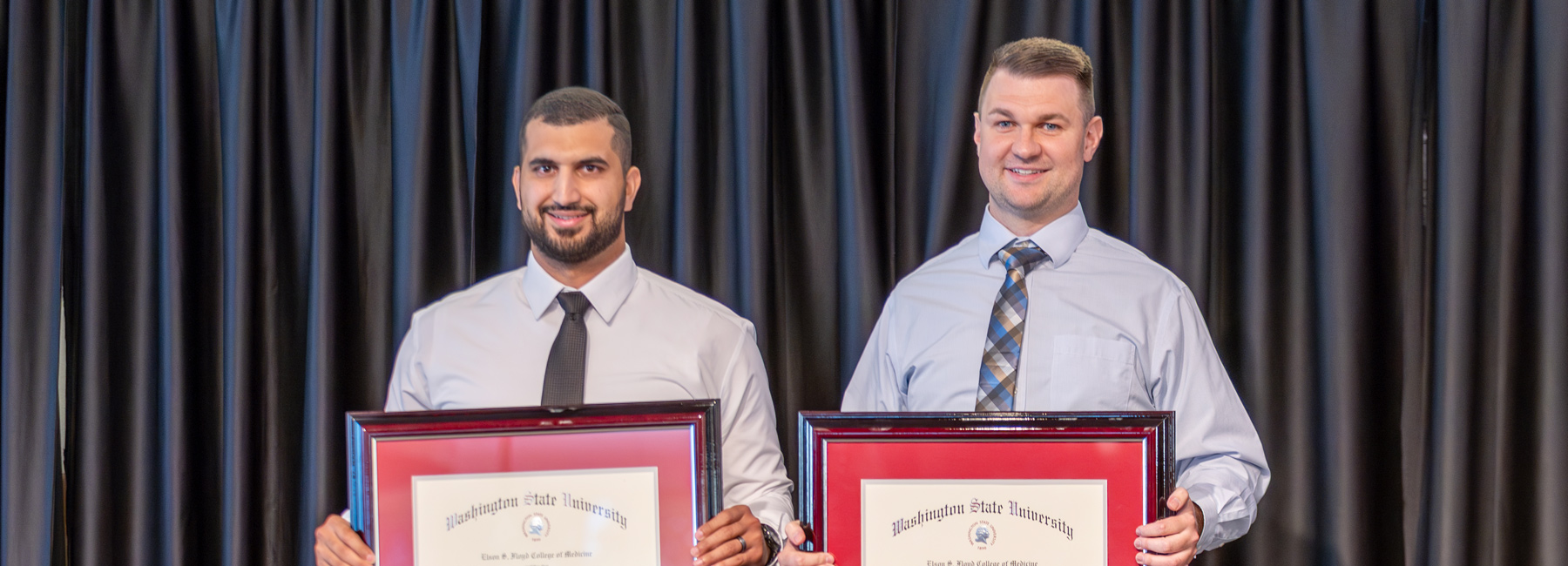 Two family medicine residents at graduation holding a framed certificate.
