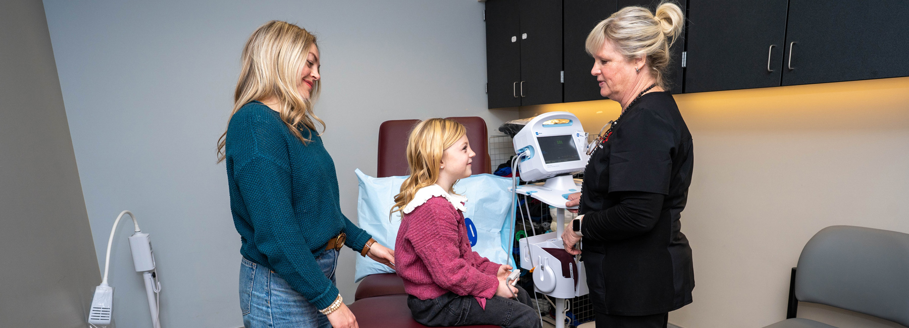 Nursing talking to child on an exam table while mom stands nearby.