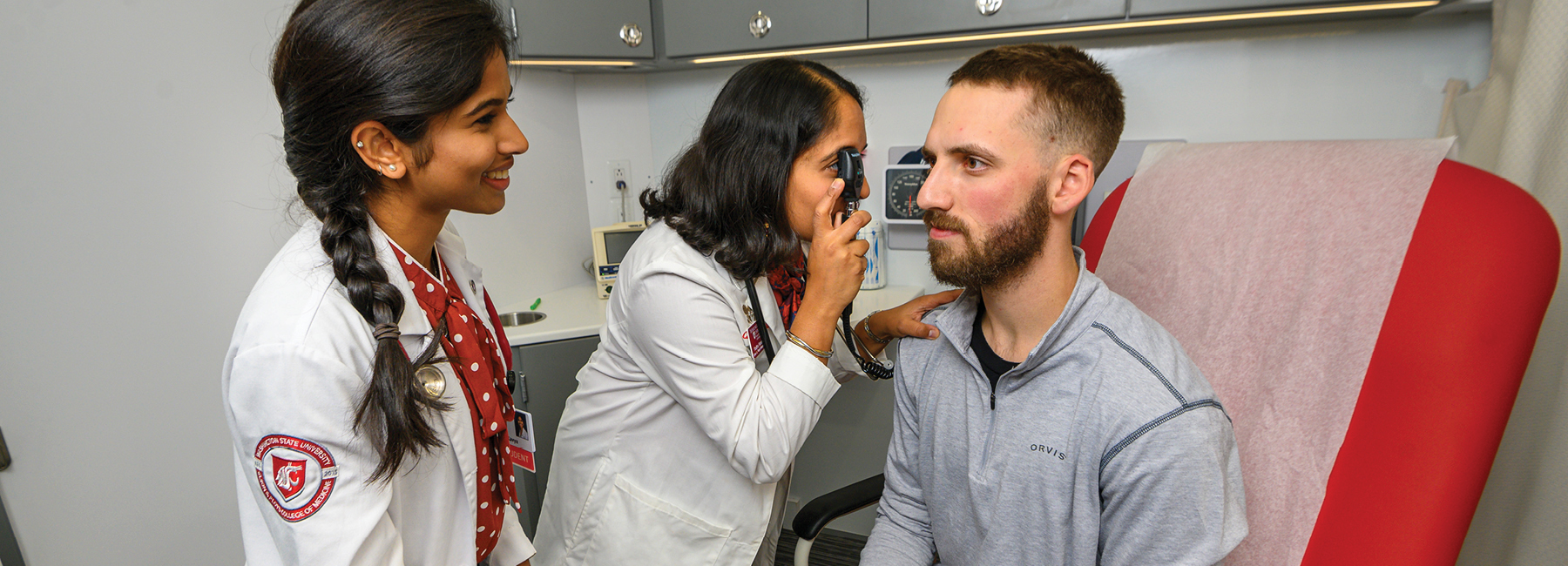 Doctor looking at a patient's eye with MD student observing.