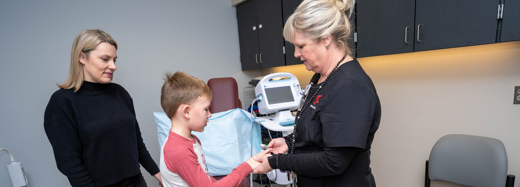 Nurse checking pulse of a child while the mom looks on.