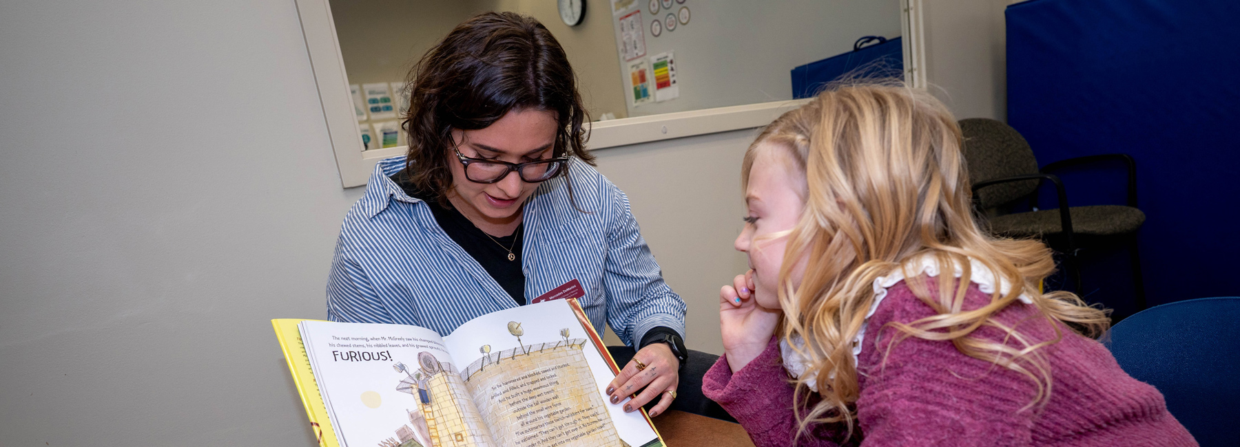 A Speech Language Pathologist with a child testing speech by reading a book.