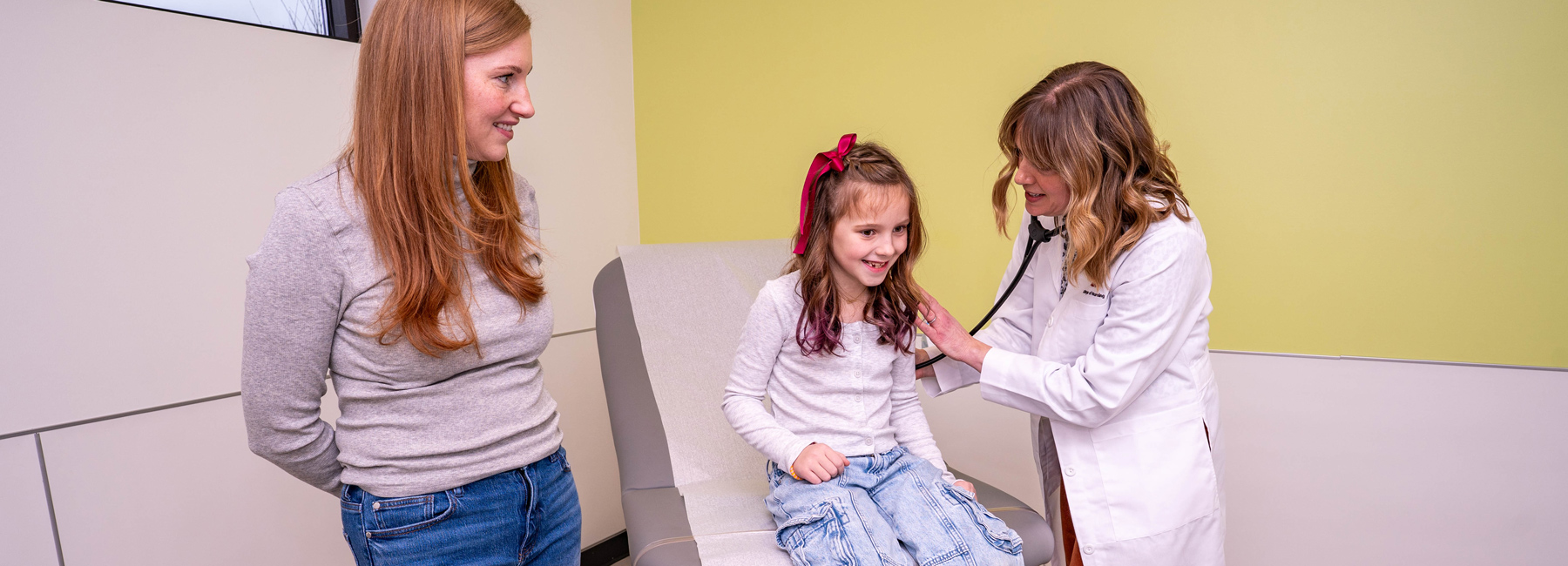 Child having an exam with a nurse as her mom watches.