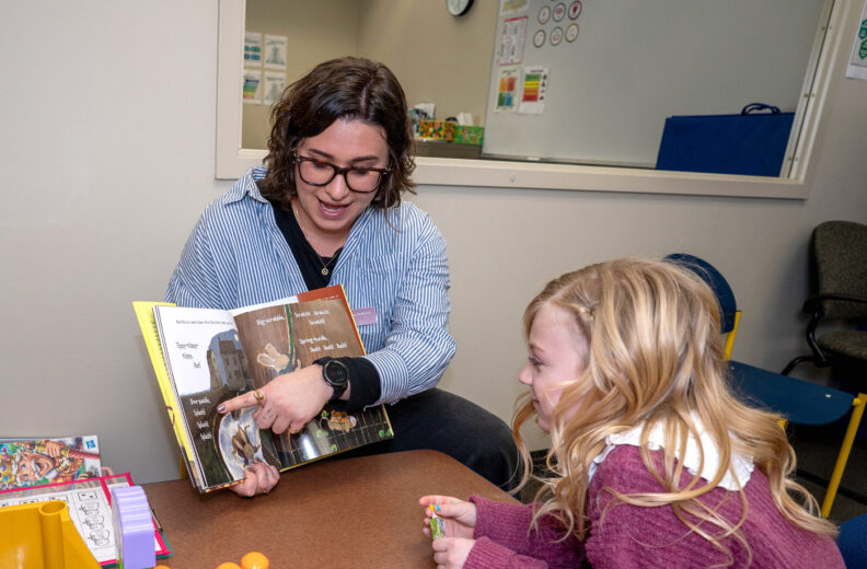 SLP working with a child reading a book in the SLP clinic.