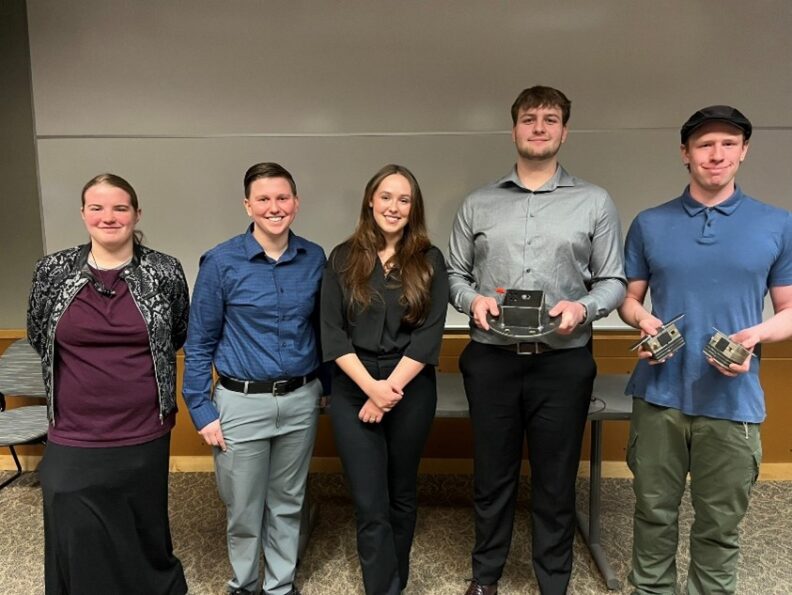 5 people posing together with two people holding components of an experiment.