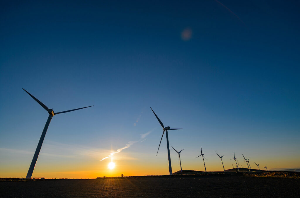 A row of windmills shown against a colorful sunset.