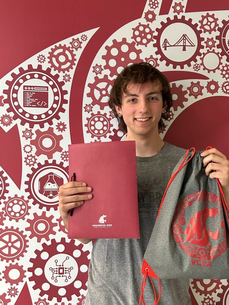 A person holds a crimson folder and a drawstring bag in front of a wall decorated with technology-themed icons.